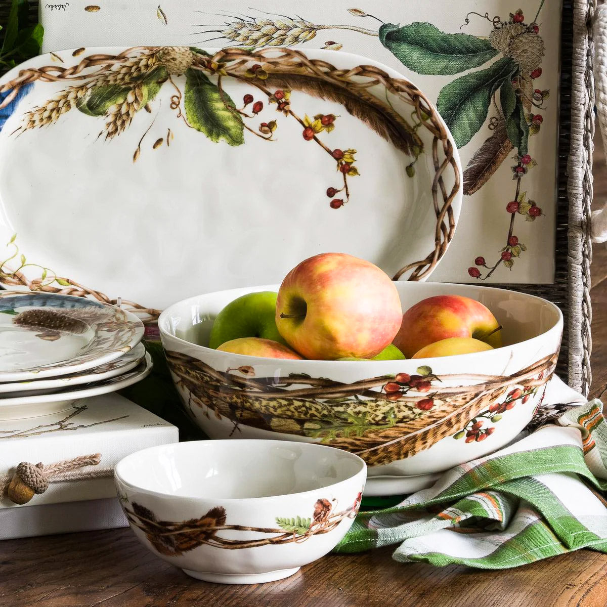 Forest Walk 10 inch serving bowl holding apples, with a platter and smaller bowl on a white table