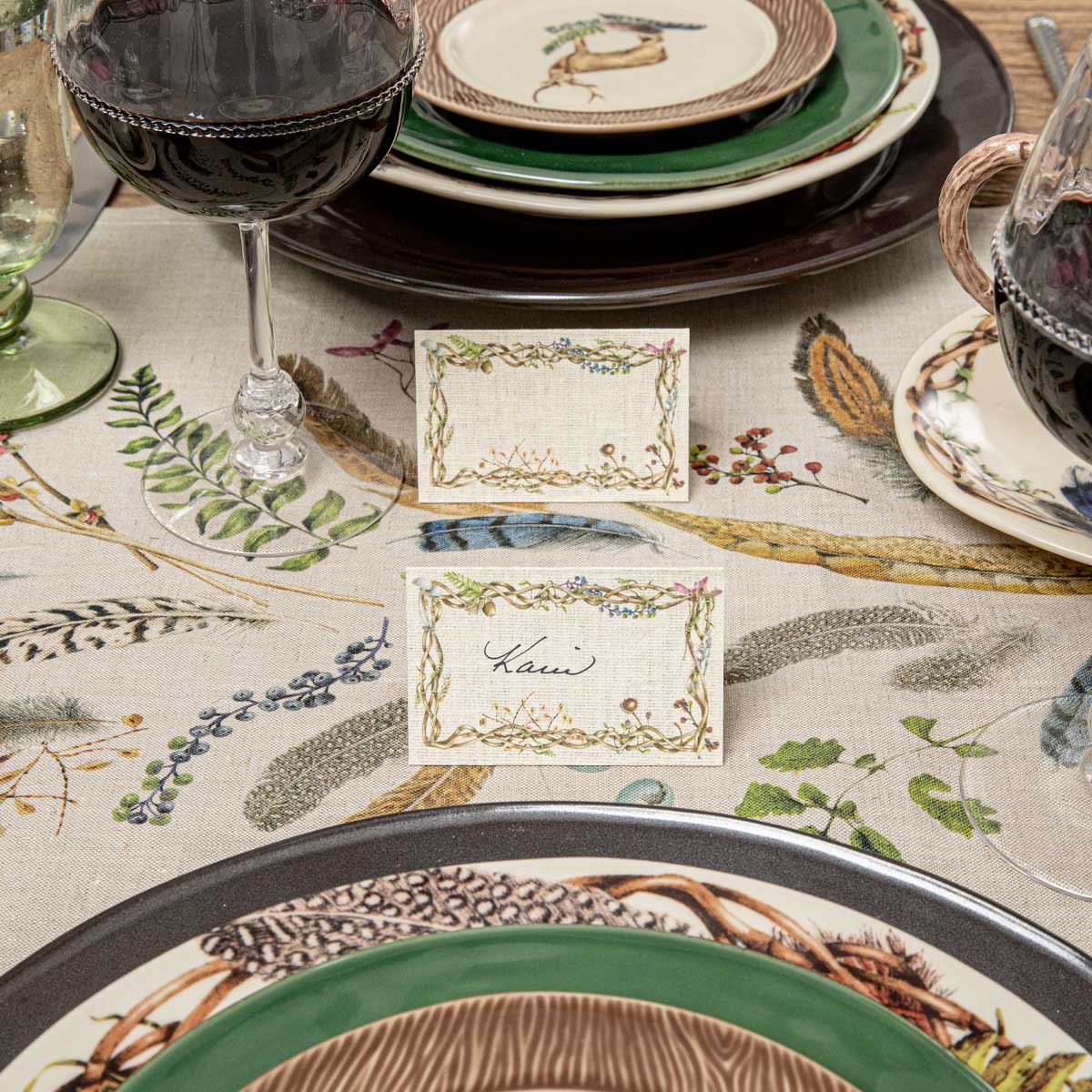 Twig border place cards at Forest Walk place settings on a feather print tablecloth