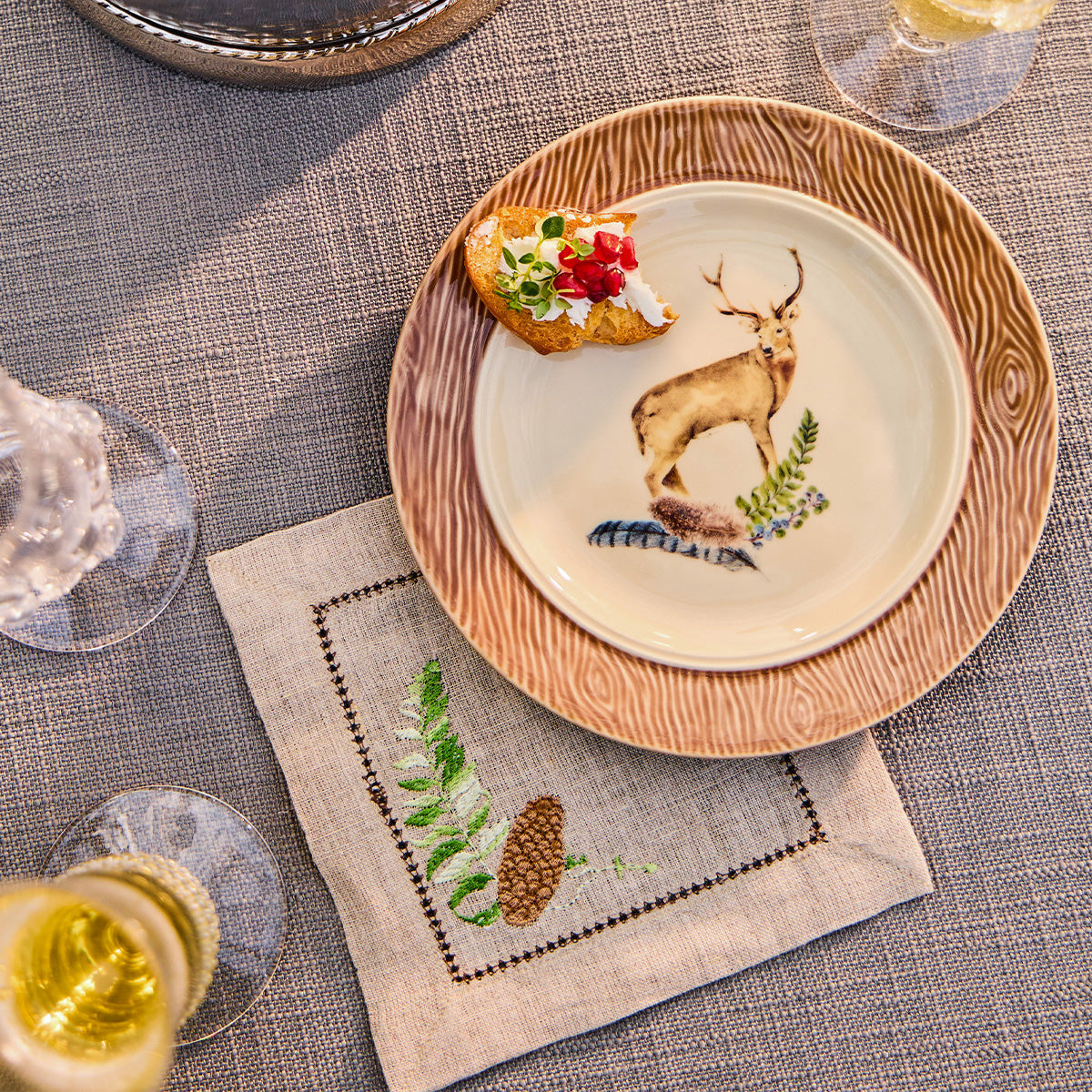 Forest Walk cocktail napkin with embroidered fern and pinecone beside a stag plate of appetizers