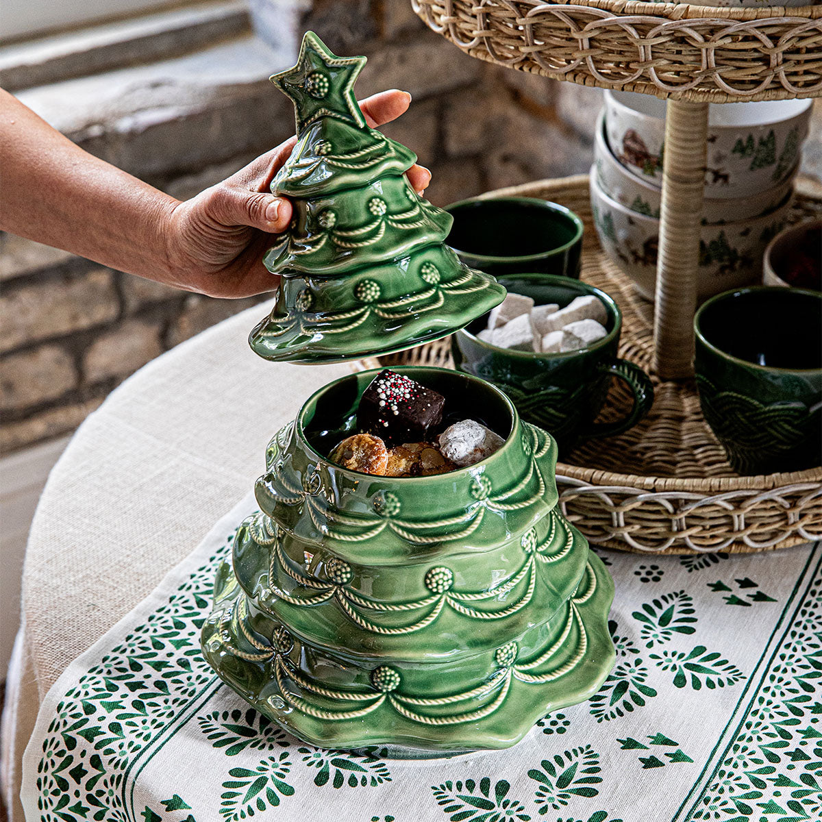Hand lifting the lid of a basil Christmas tree cookie jar filled with treats