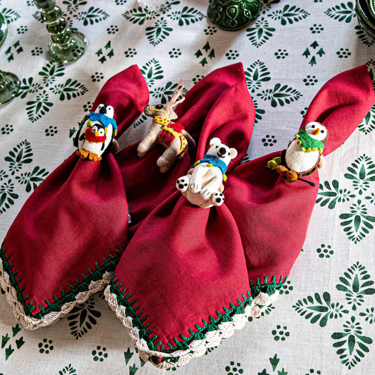 Red napkins gathered in North Pole felt animal napkin rings on a green and white tablecloth