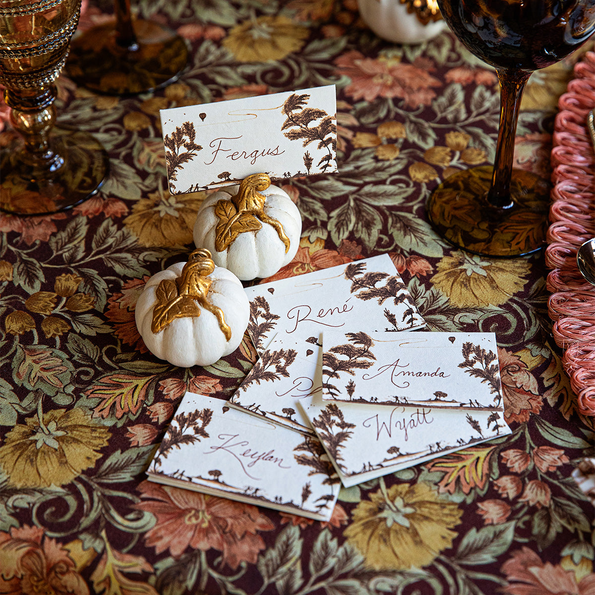White and gold Forest Walk pumpkin place card holders with name cards on a floral tablecloth