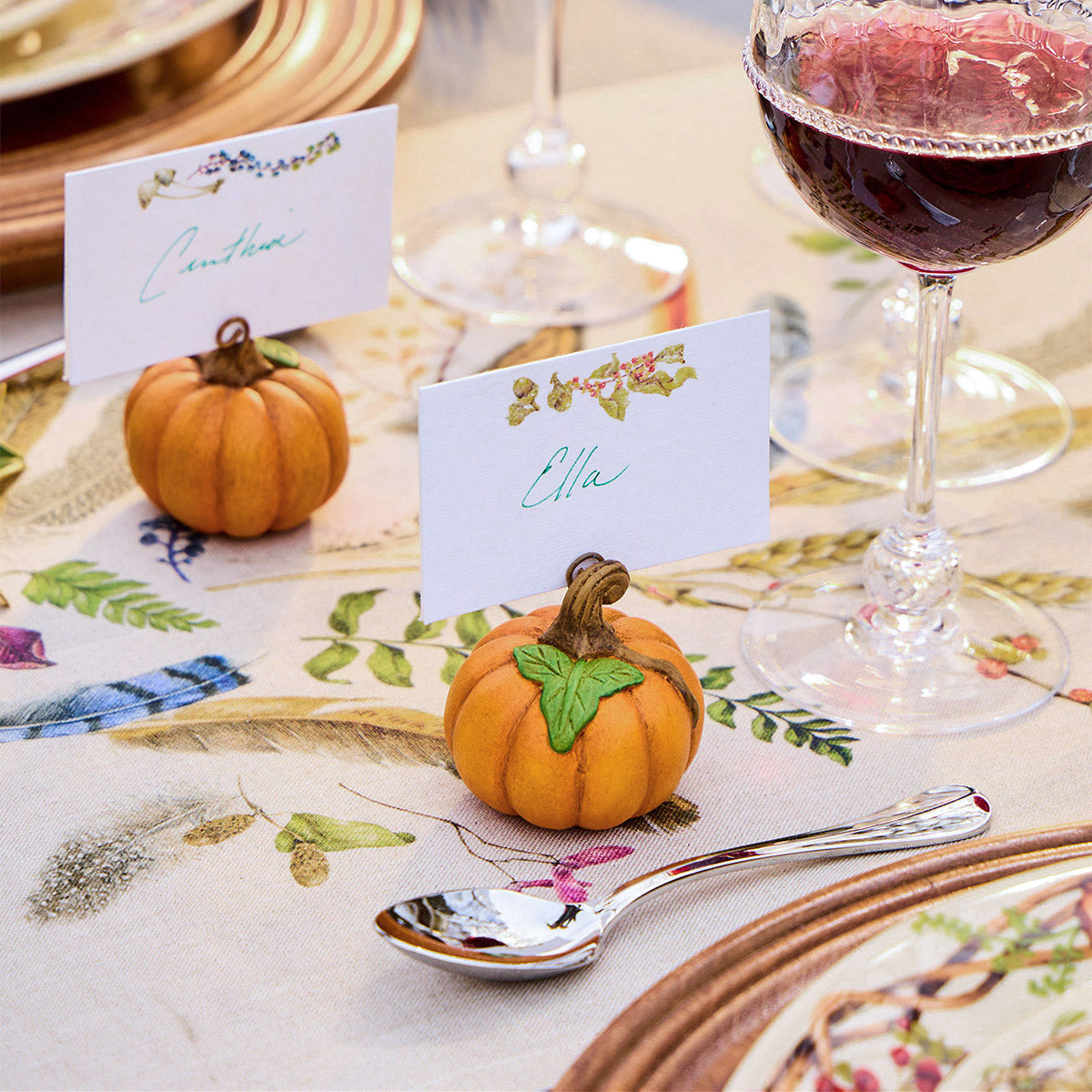 Orange Forest Walk pumpkin place card holders with name cards on a feather print tablecloth beside wine glasses