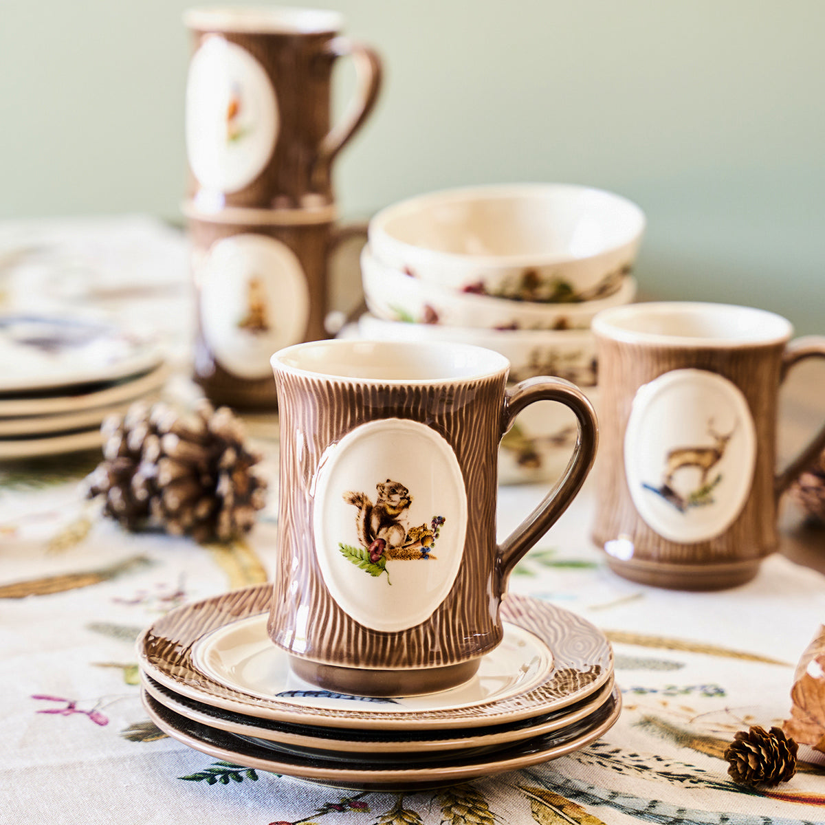 Forest Walk squirrel mug on stacked saucers with more animal mugs and pinecones on a patterned tablecloth
