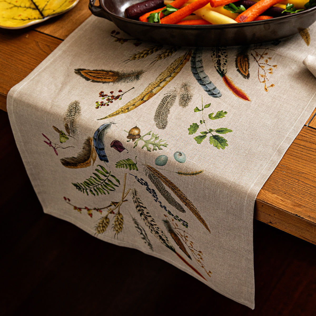 Forest Walk 18 by 90 inch table runner with feather print on a dark wood table with a skillet of vegetables