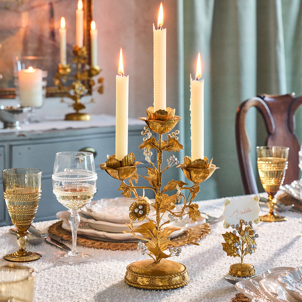 Gold holly candelabra with lit tapers on a table set with amber glassware and white plates