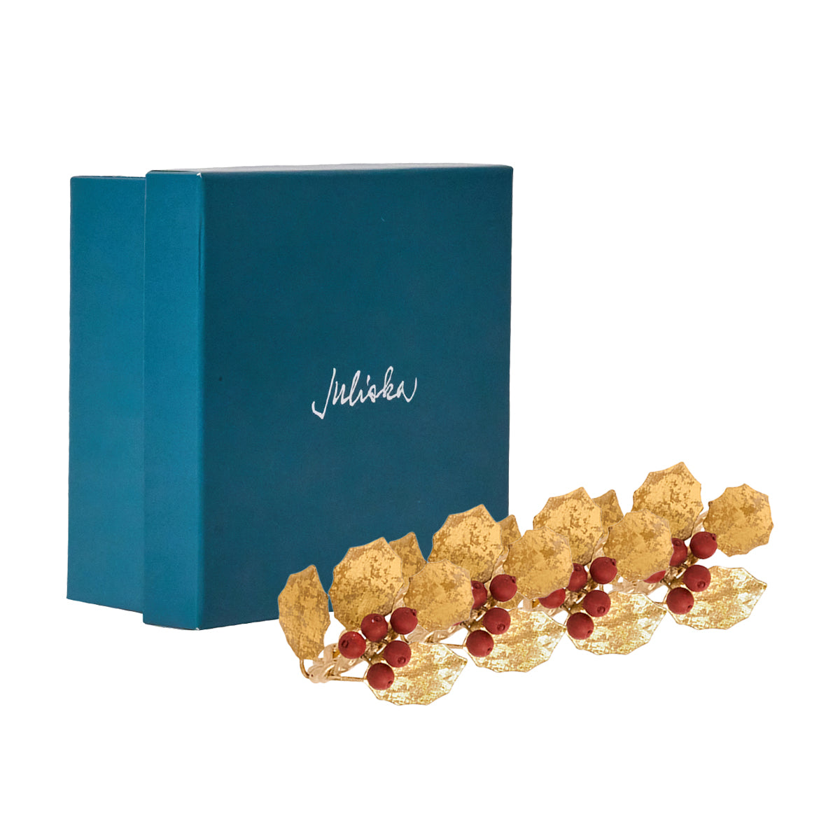 Juliska Forest Walk gold holly napkin rings with red berries in front of a teal gift box
