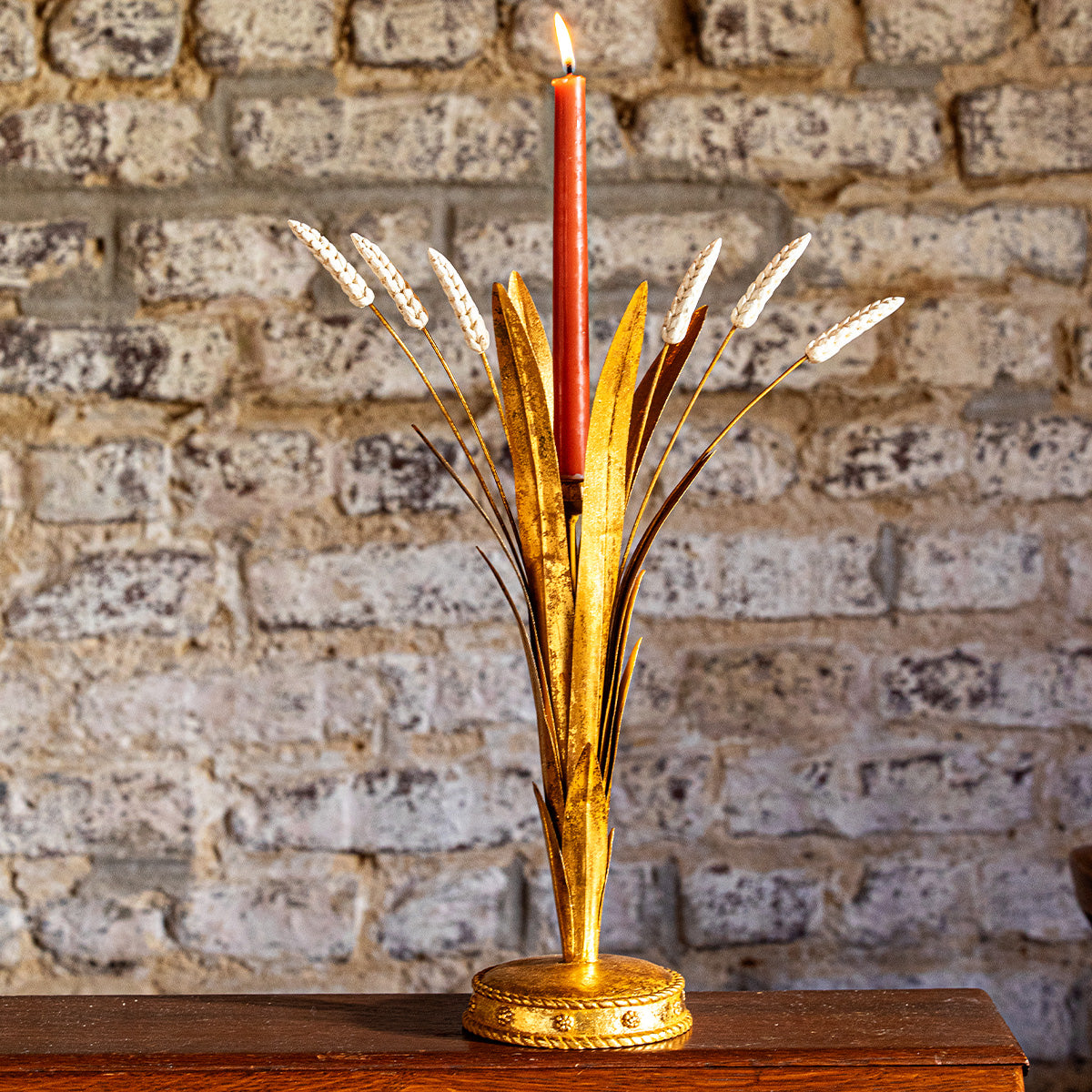 Forest Walk 17 inch gold wheat candlestick holder with a red taper against a brick wall