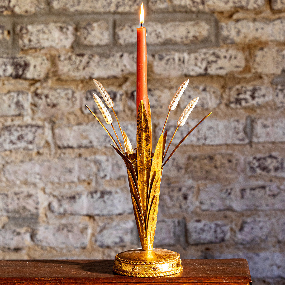 Forest Walk 13 inch gold wheat candlestick holder with a red taper against a brick wall
