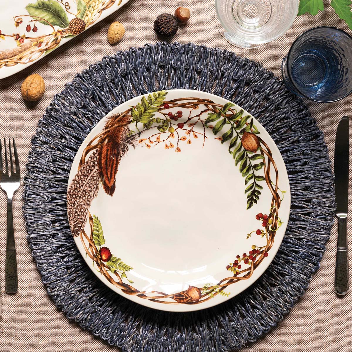 Forest Walk dinner plate on a dark woven round placemat with silverware and glasses
