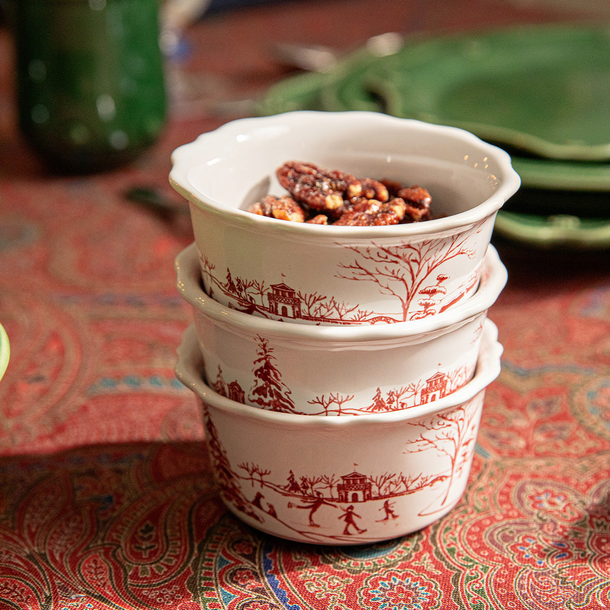 Stacked ruby Winter Frolic ramekins holding pecans on a paisley tablecloth