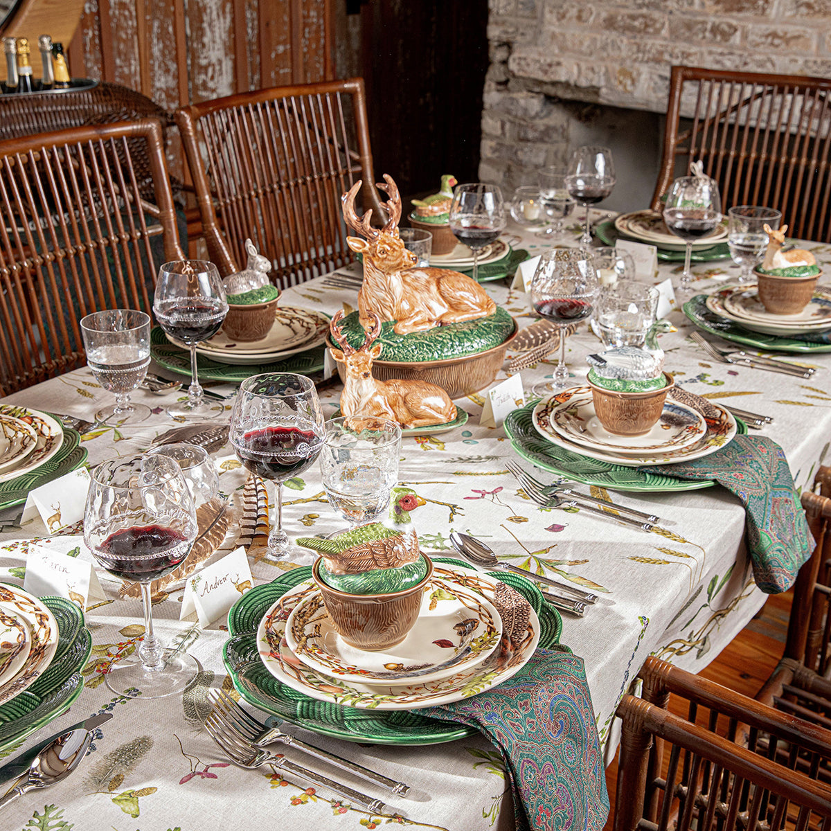 Forest Walk 60 by 120 inch tablecloth on a dining table set with green chargers and a stag centerpiece