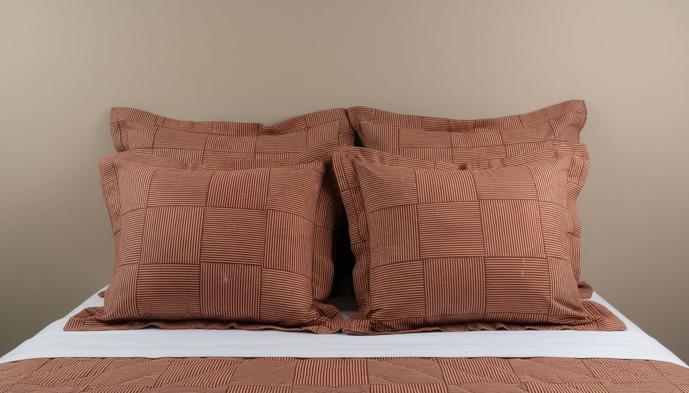 Four terracotta Henry Handwork Wabi Sabi pillow shams with grid stitching on a made bed.