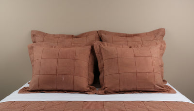 Four terracotta Henry Handwork Wabi Sabi pillow shams with grid stitching on a made bed.