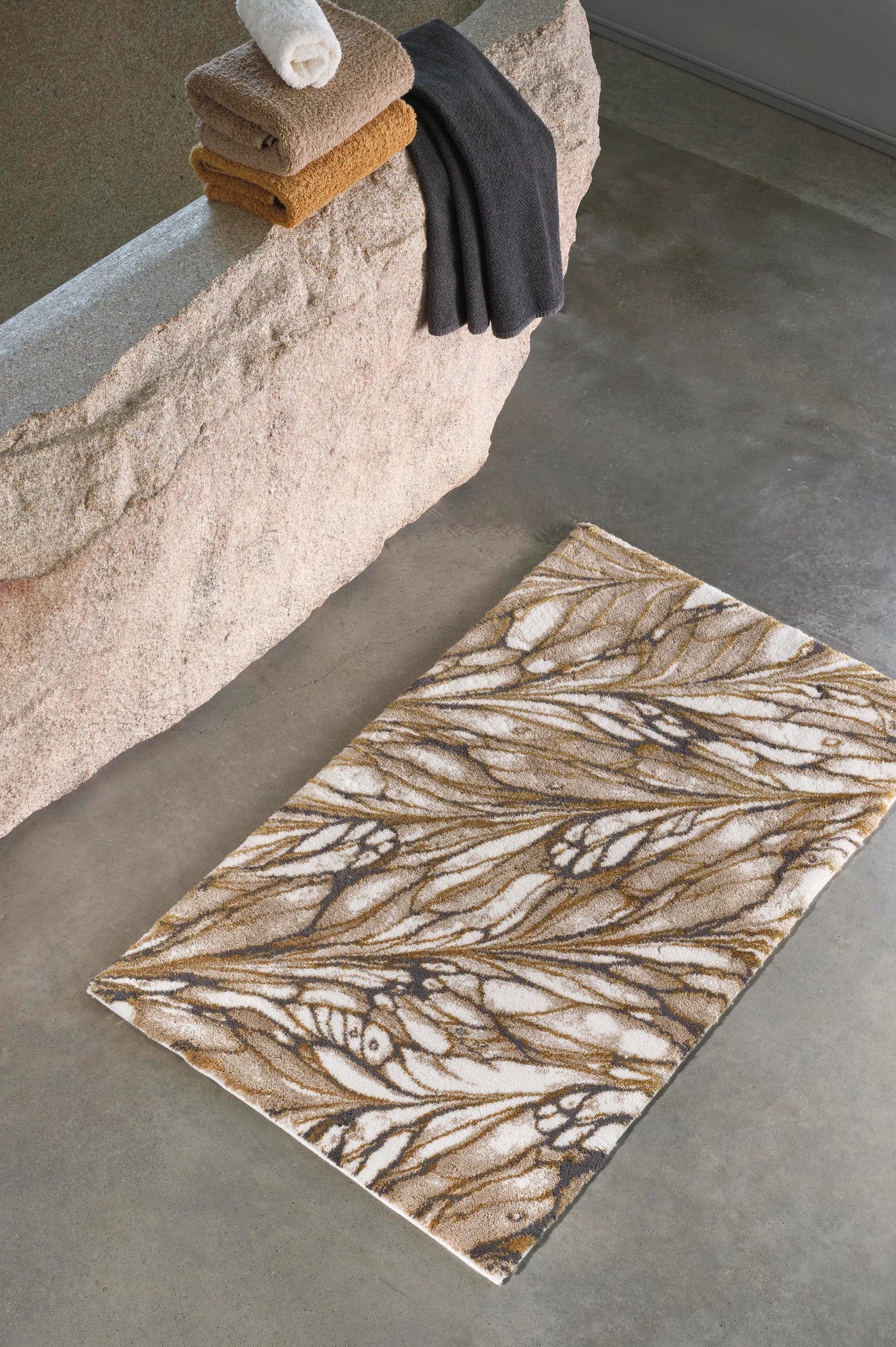Close-up overhead view of Diane bath rug with ivory and camel leaf pattern on concrete floor.