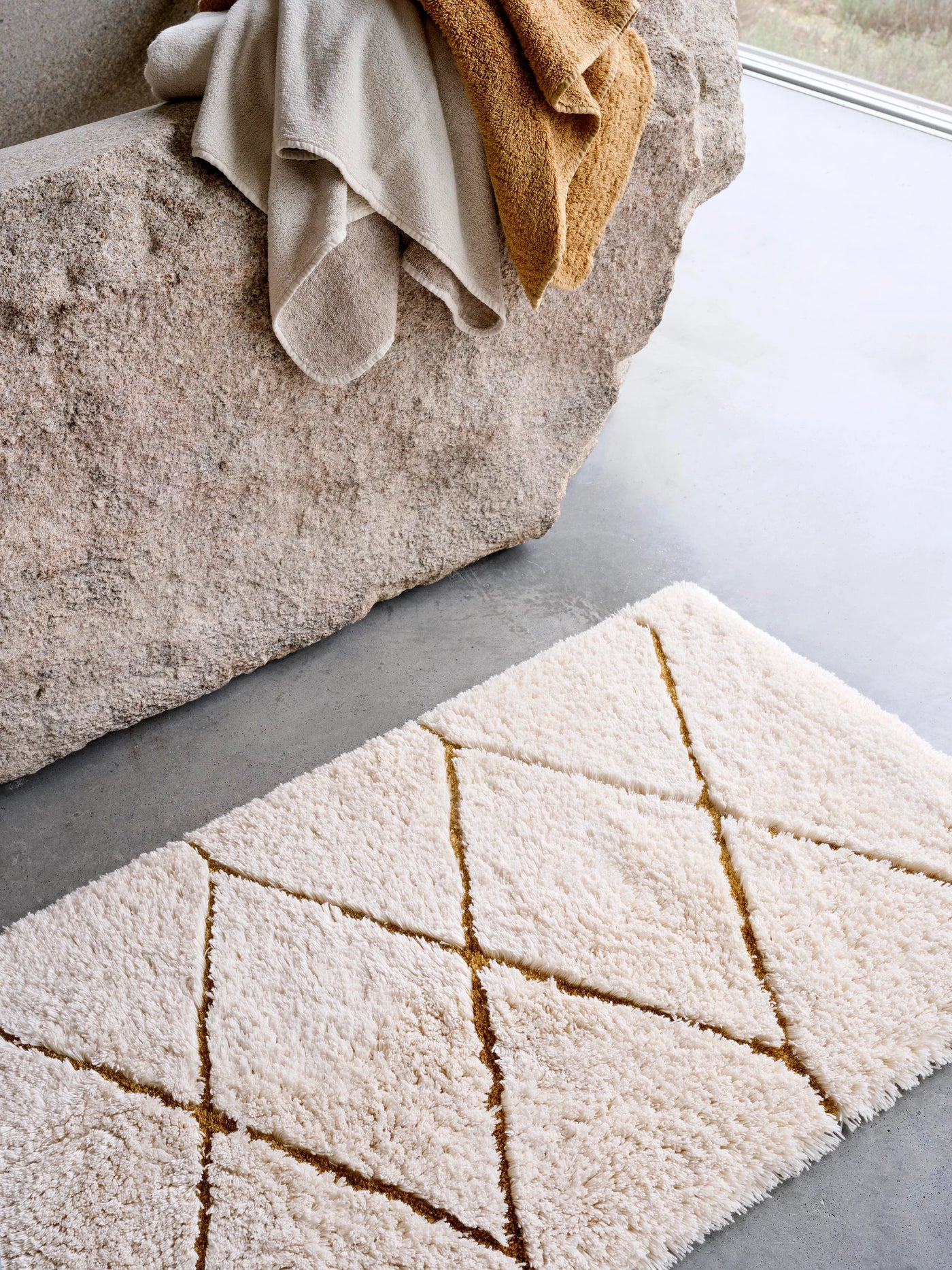 Abyss Habidecor Heritage ivory bath rug with gold diamond trellis pattern on concrete floor.