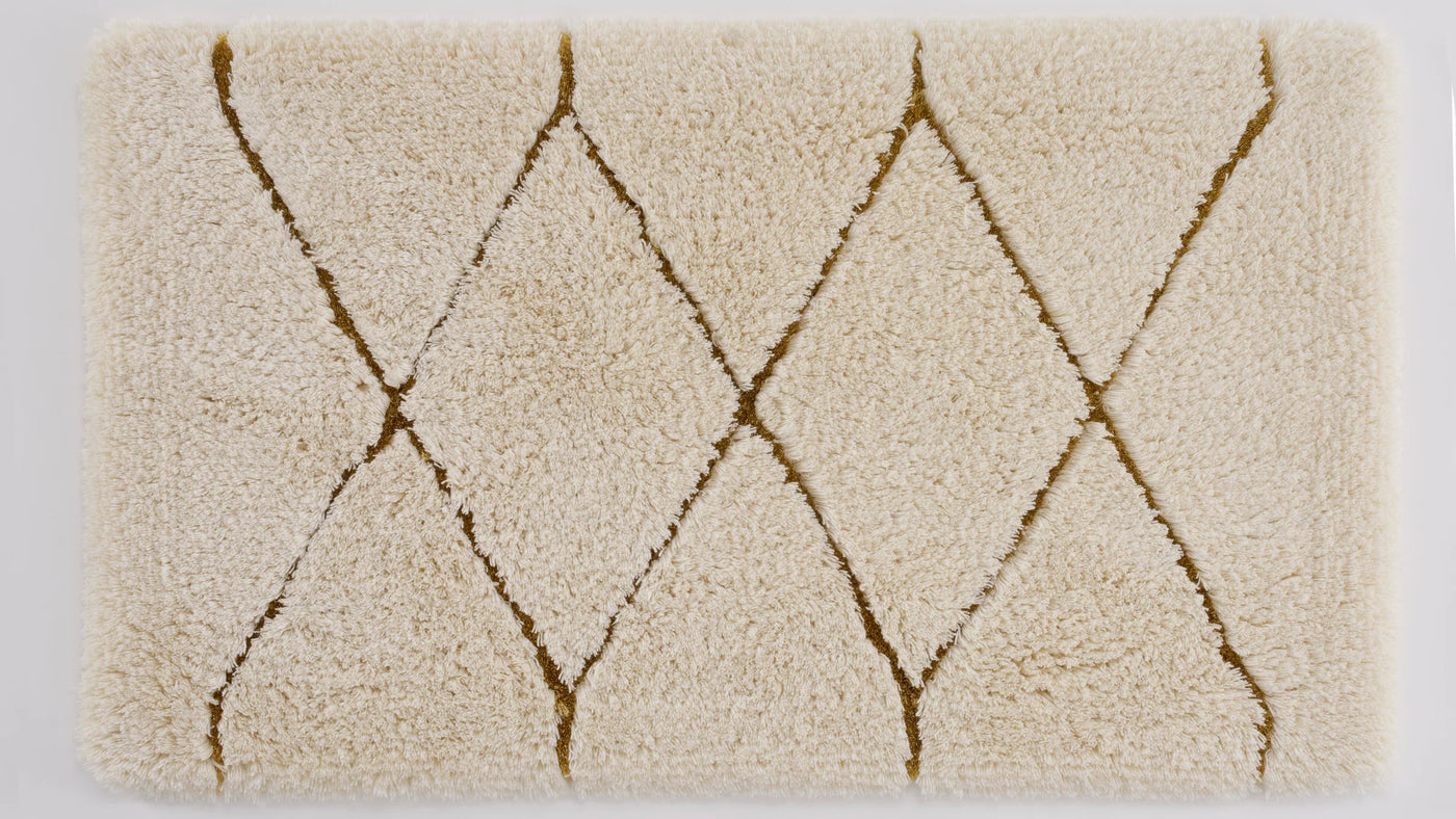 Close-up of Abyss Habidecor Heritage bath rug with ivory pile and gold diamond pattern.