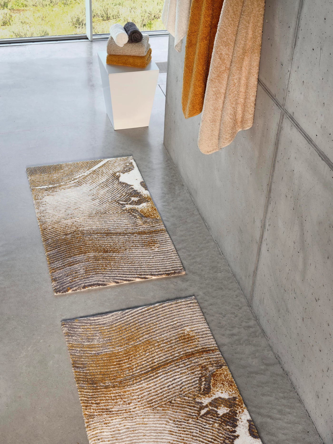 Abyss Habidecor Lana bath rugs in gold and ivory marbled pattern on concrete floor.