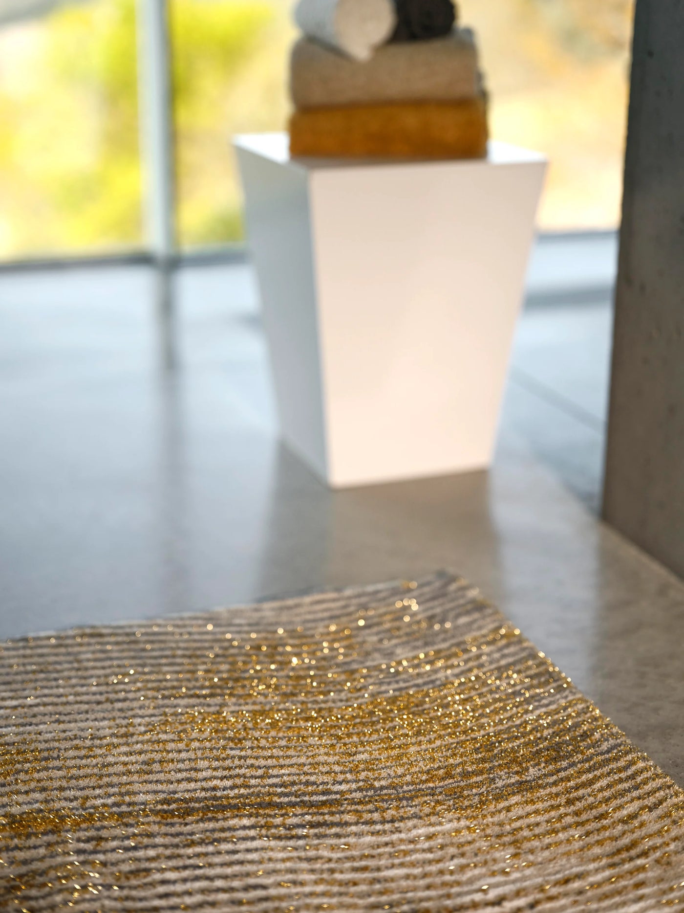 Close-up of Abyss Habidecor Lana rug showing gold metallic stripe texture on stone surface.