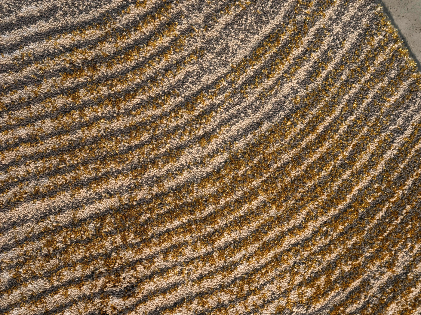 Close-up of Abyss Habidecor Lana rug showing curved gold and taupe wool stripe texture.