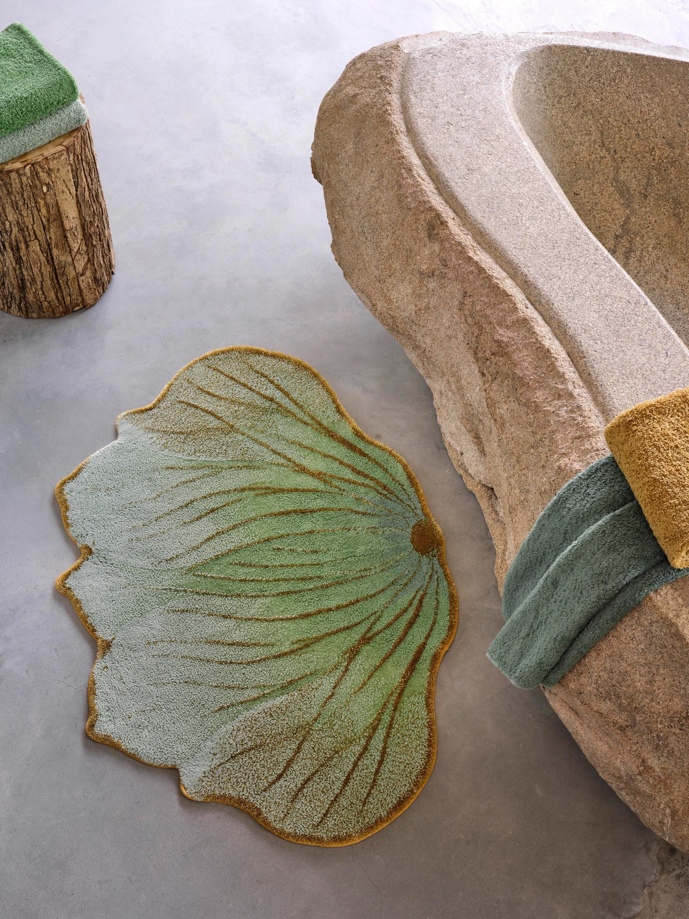 Close-up of Abyss Habidecor Lotus rug's sage and gold leaf shape on stone surface.