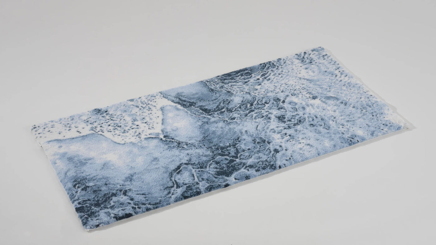 Close-up of Abyss Habidecor Nazare rug showing ocean wave pattern in slate blue and white.