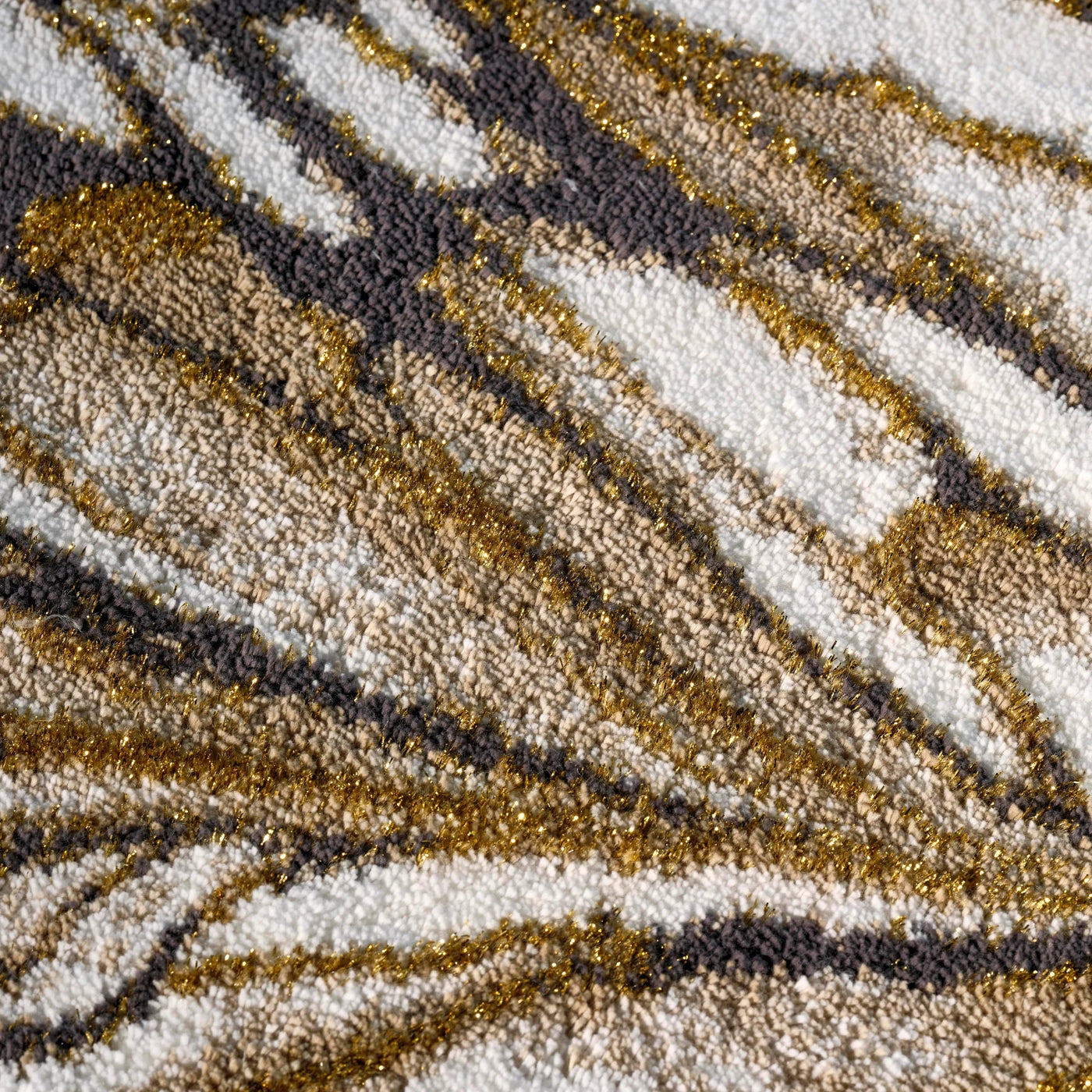 Close-up of Abyss Habidecor Diane rug texture, gold and charcoal wave pattern on ivory.