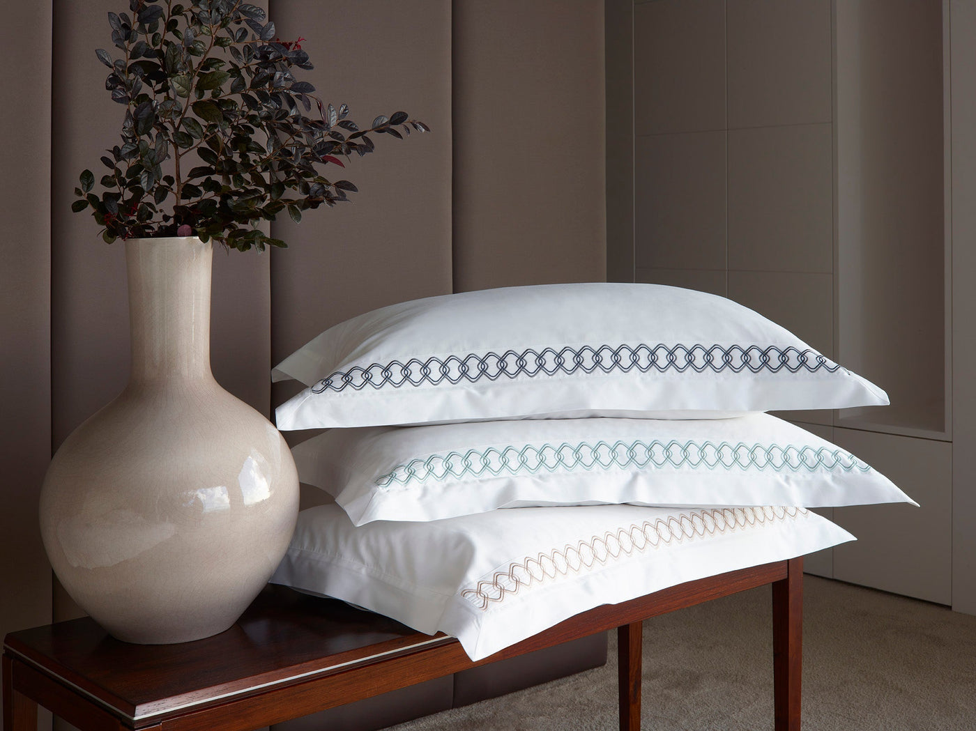 Close-up of stacked white Ornato euro shams showing varied embroidered border colorways.
