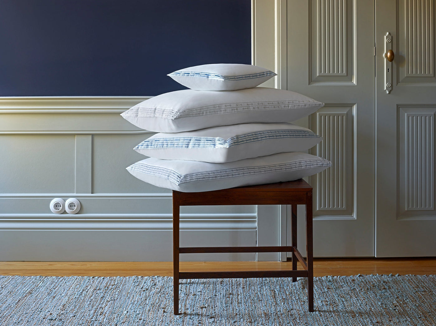 Stack of pillows on a wooden stool in a room with a blue wall and white door.