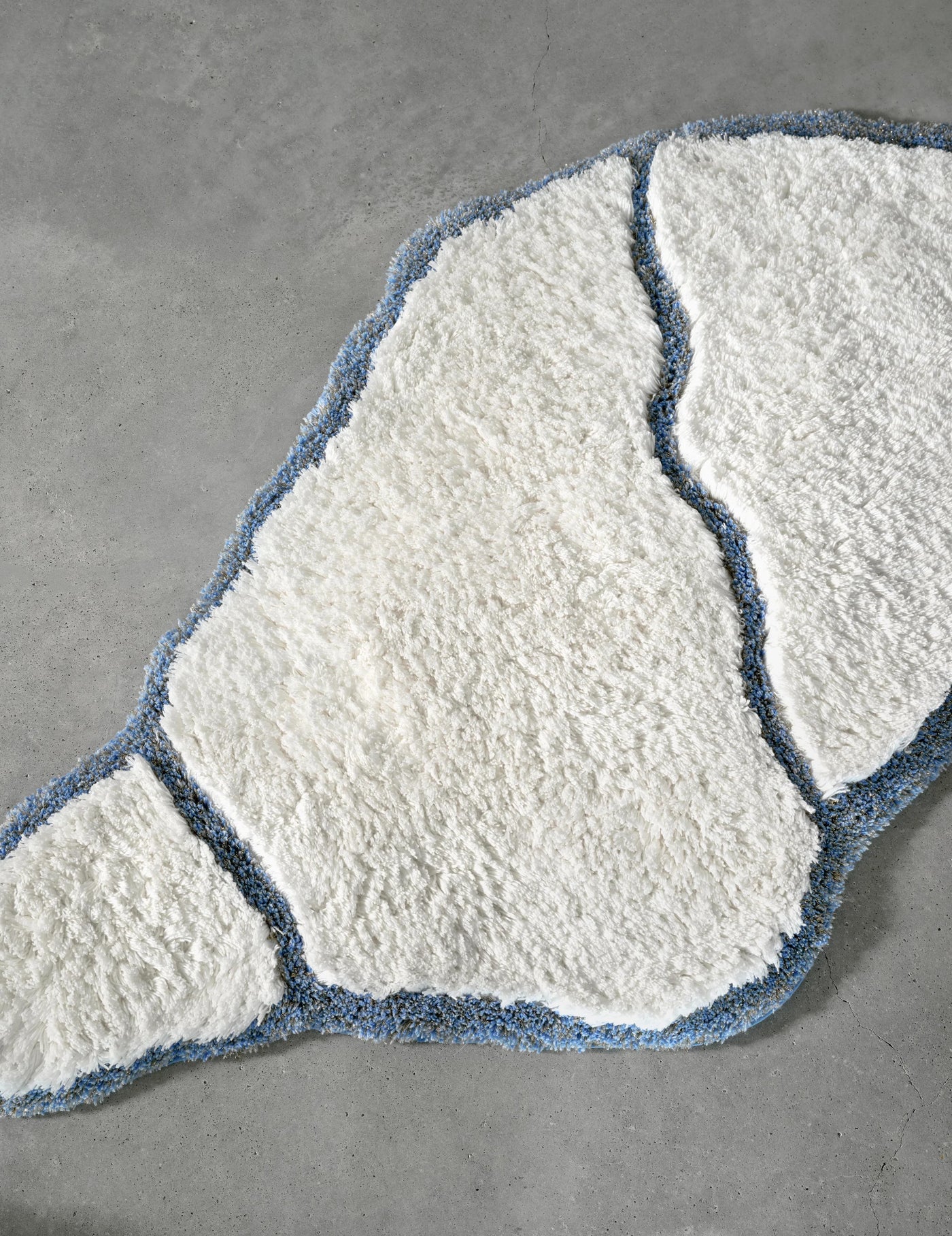 Overhead view of ivory tufted bath rug with slate blue border on grey surface.