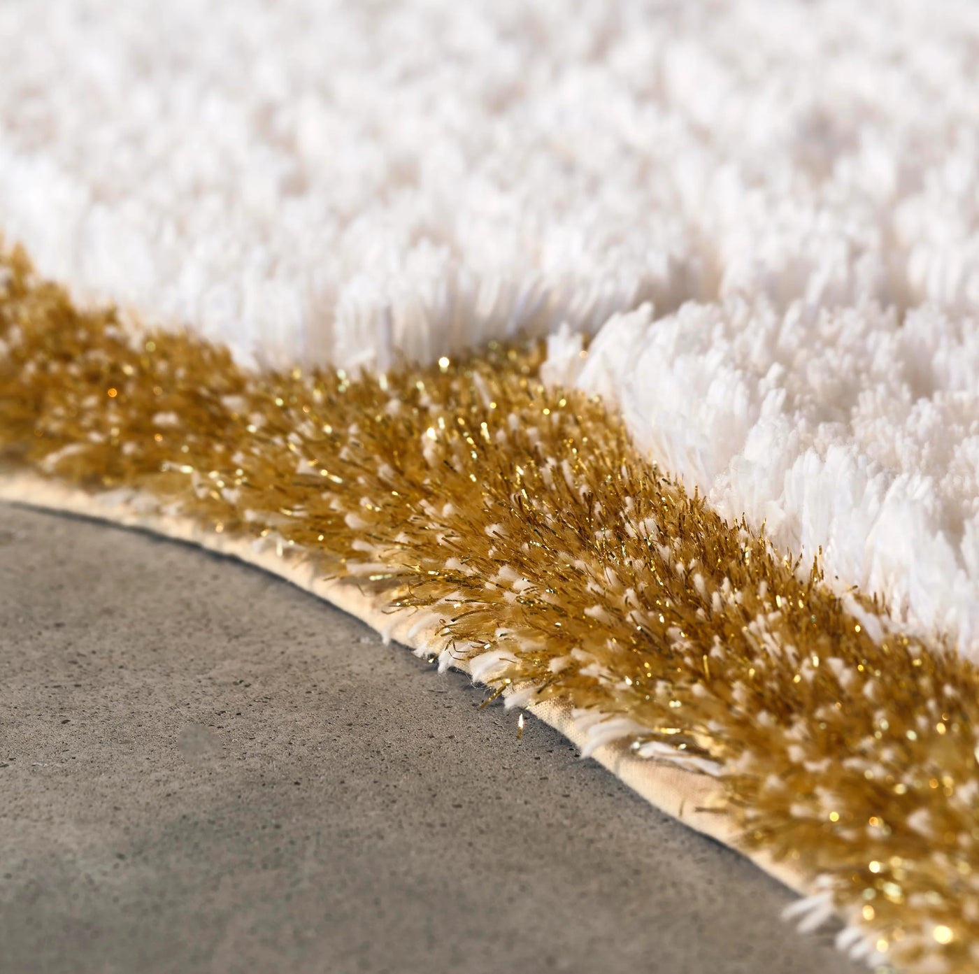 Close-up of ivory terry pile meeting a gold lurex border on a bath rug edge.