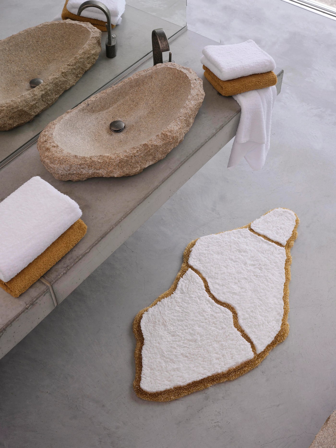 Abyss Habidecor Jess bath rug in white and mustard abstract shape on concrete floor.
