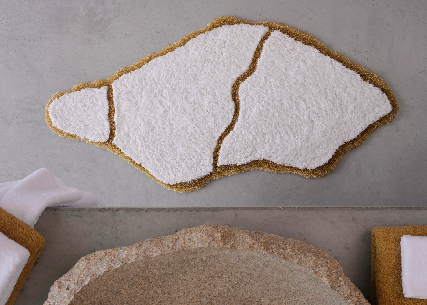 Overhead view of Abyss Habidecor Jess bath rug in white with gold border on concrete floor.