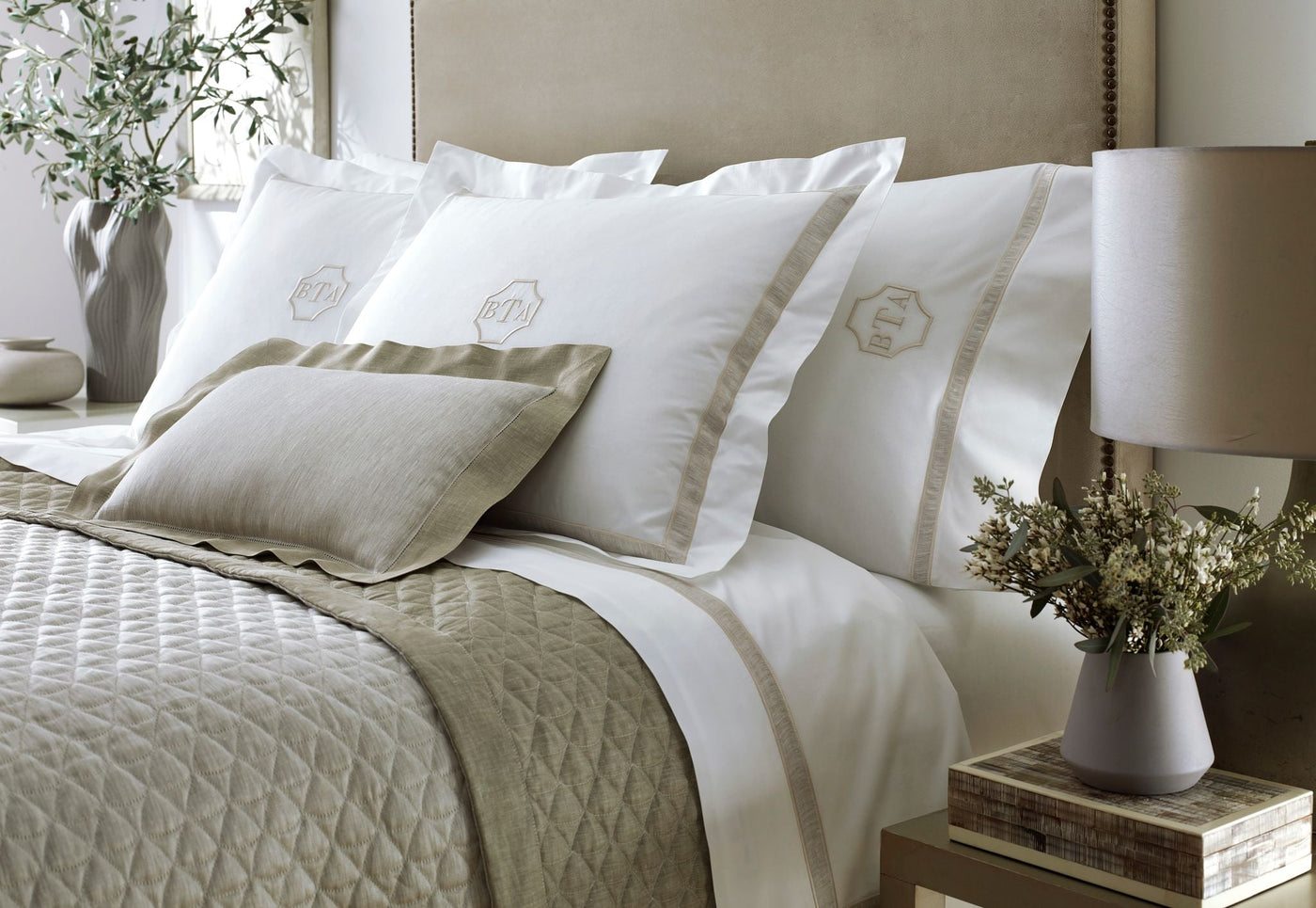 Home Treasures Alina bedding styled in white and taupe on a made bed with quilted coverlet.
