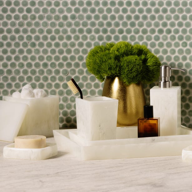 White alabaster bath accessories set styled on marble surface with penny tile backdrop.