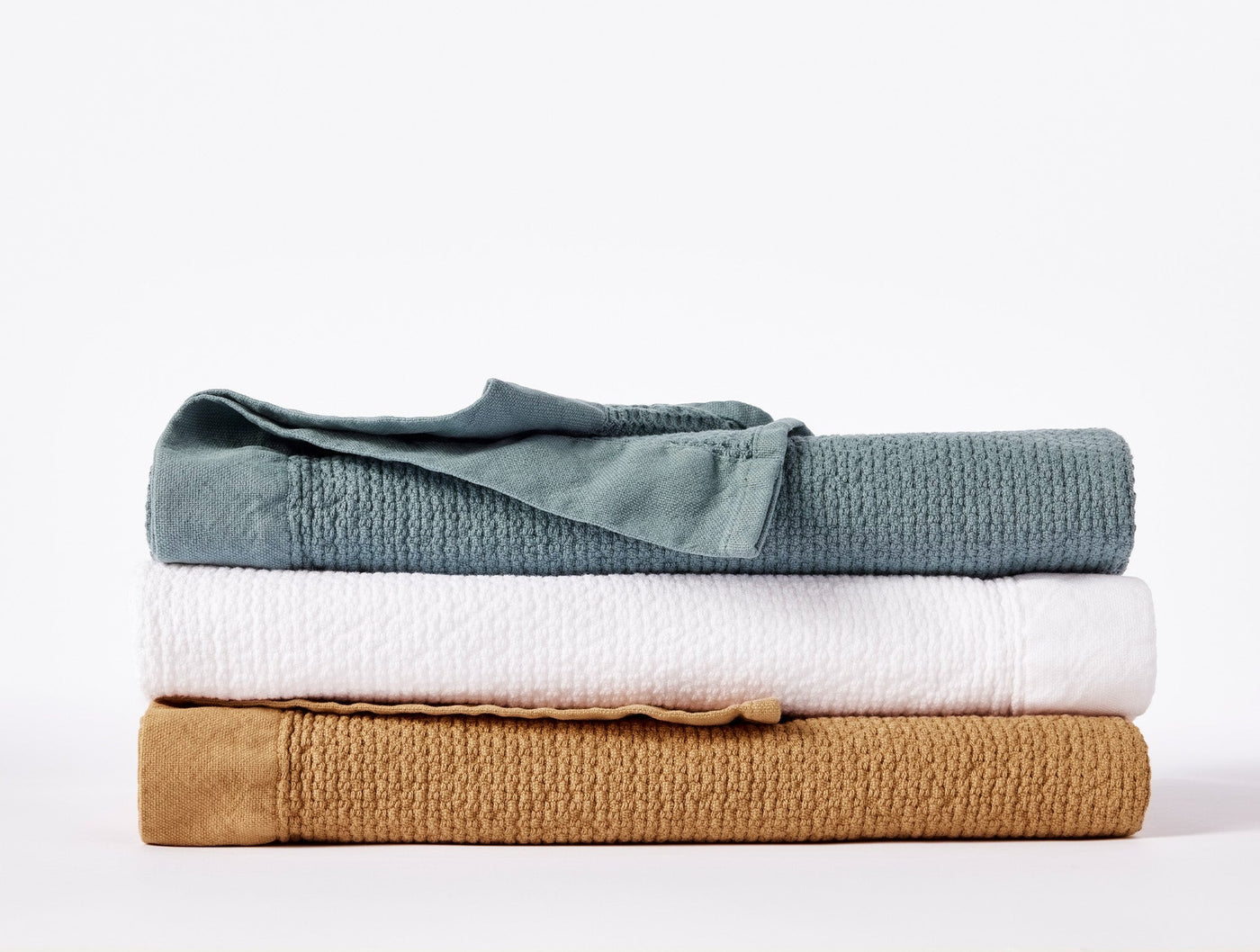 Three folded Coyuchi Adriatic towels stacked in slate, white, and amber colorways.
