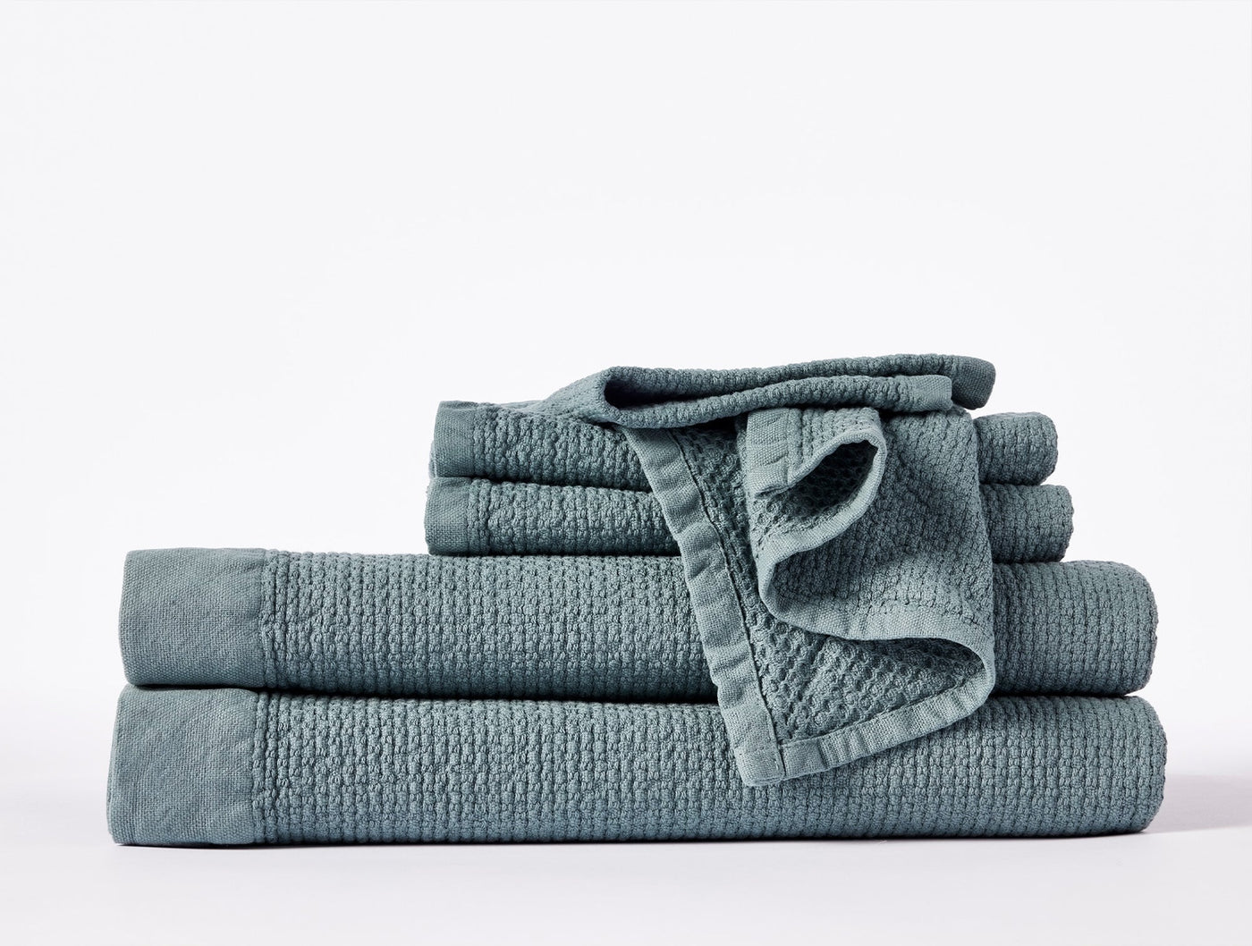 Slate blue Coyuchi Adriatic towel set stacked, showing textured weave and scalloped trim detail.