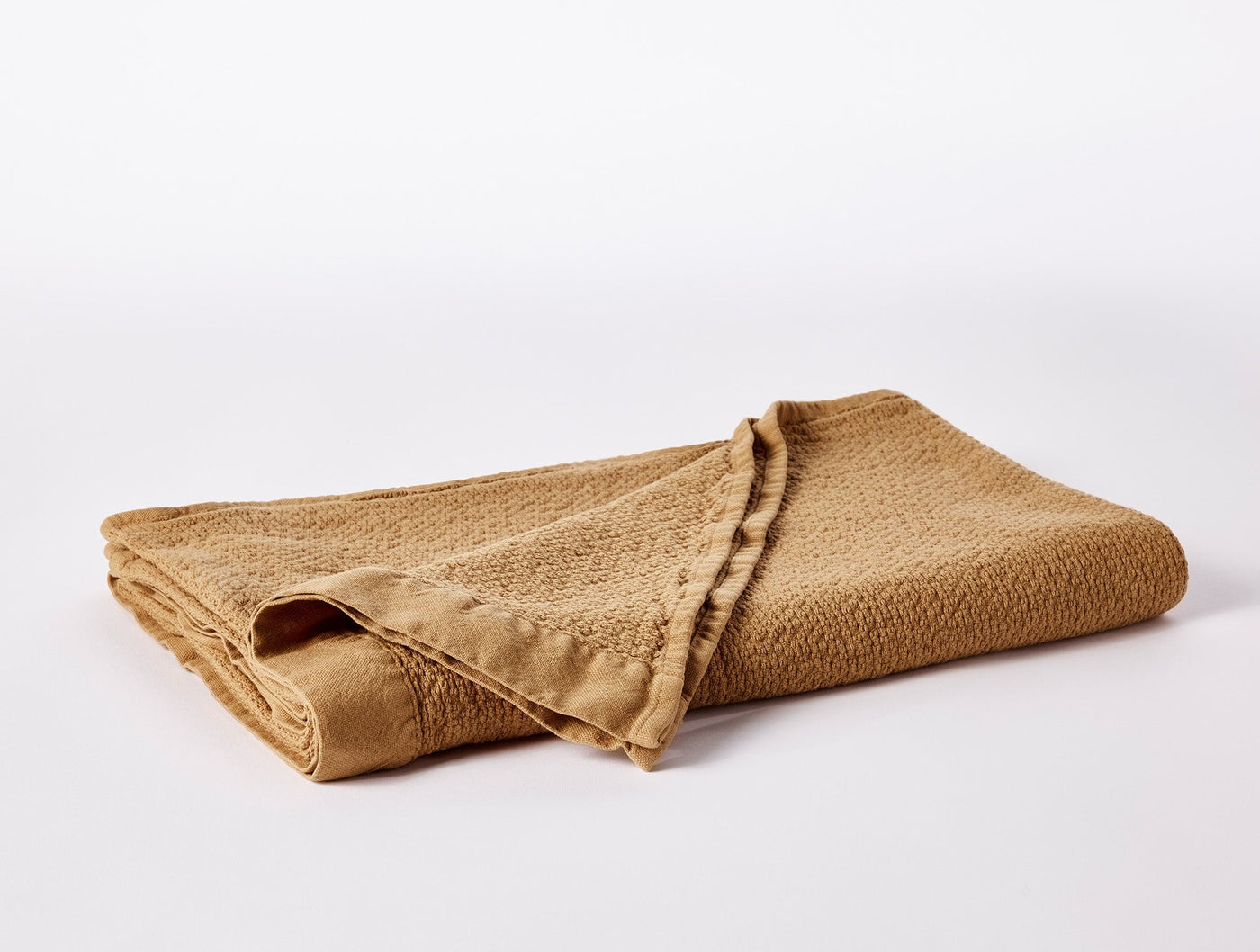 Folded honey-hued Coyuchi Adriatic towel showing textured weave and ruffled edge trim.