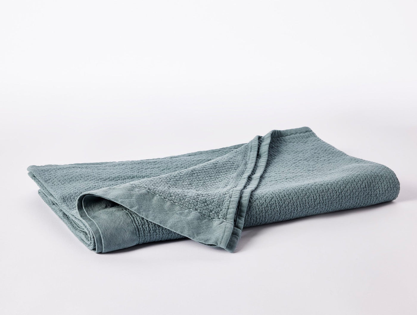 Folded sage green Coyuchi Adriatic wash cloth showing textured weave surface detail.