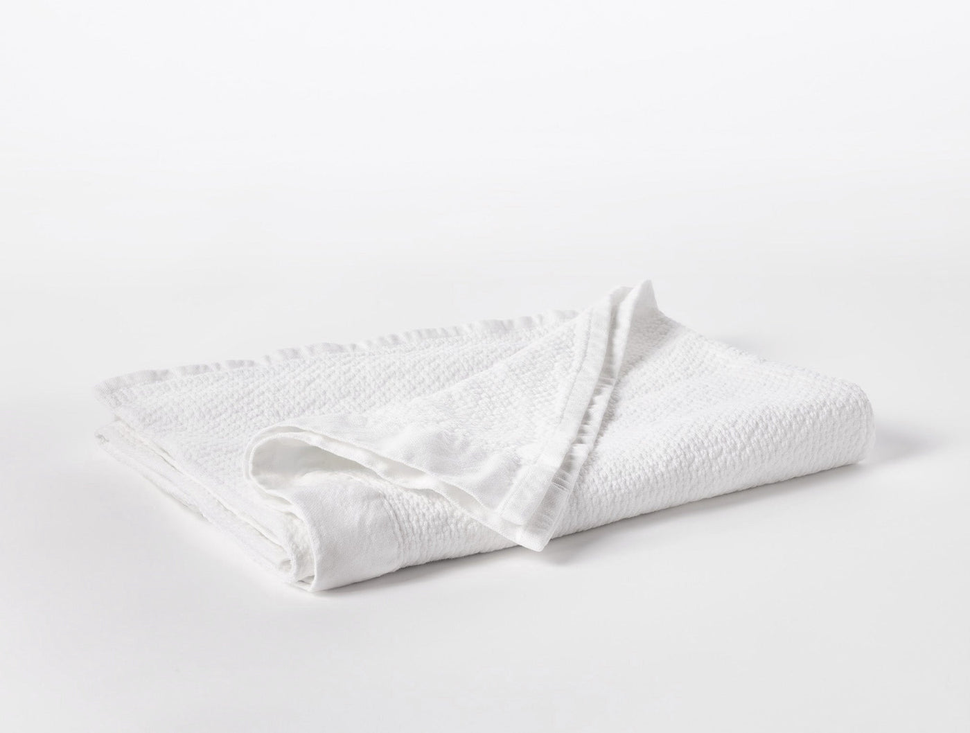 Folded white Coyuchi Adriatic towel showing textured weave and fringe trim detail.