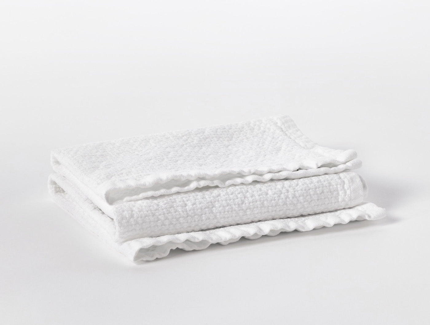Folded white waffle-weave towels with scalloped edges stacked on a light surface.