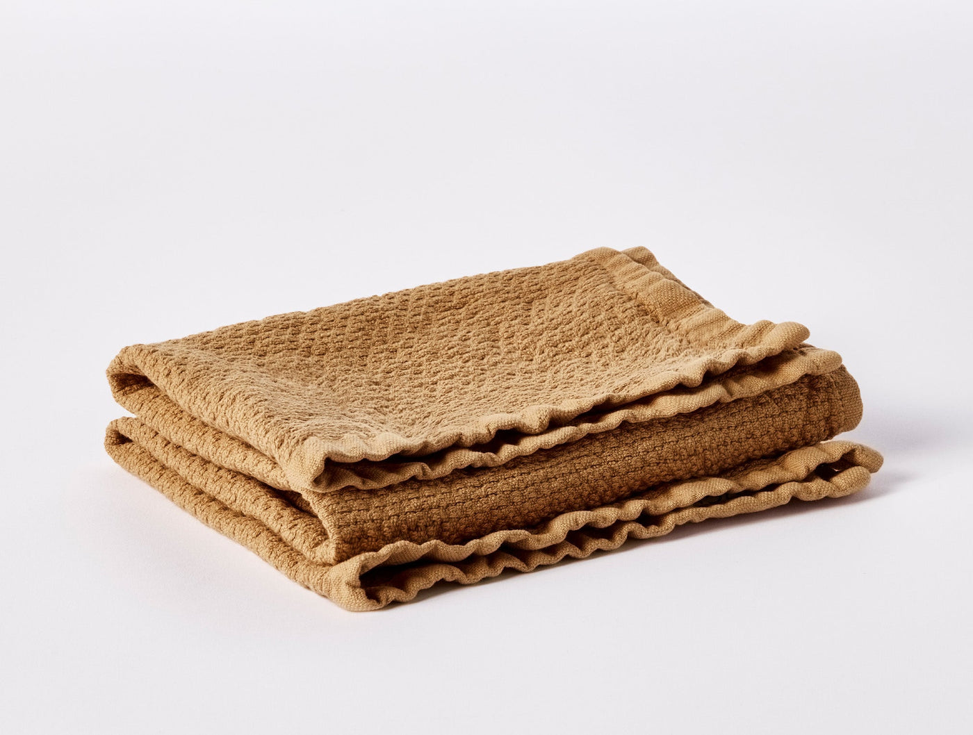 Close-up of folded caramel waffle-weave guest towel with ruffled edges.