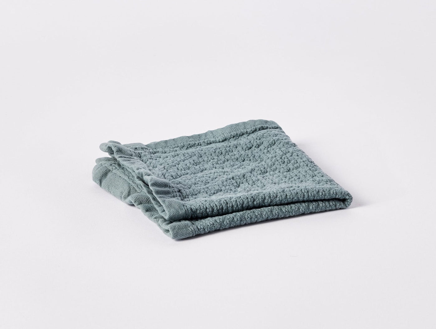 Folded sage green terry towel showing ribbed texture and fringe trim detail.