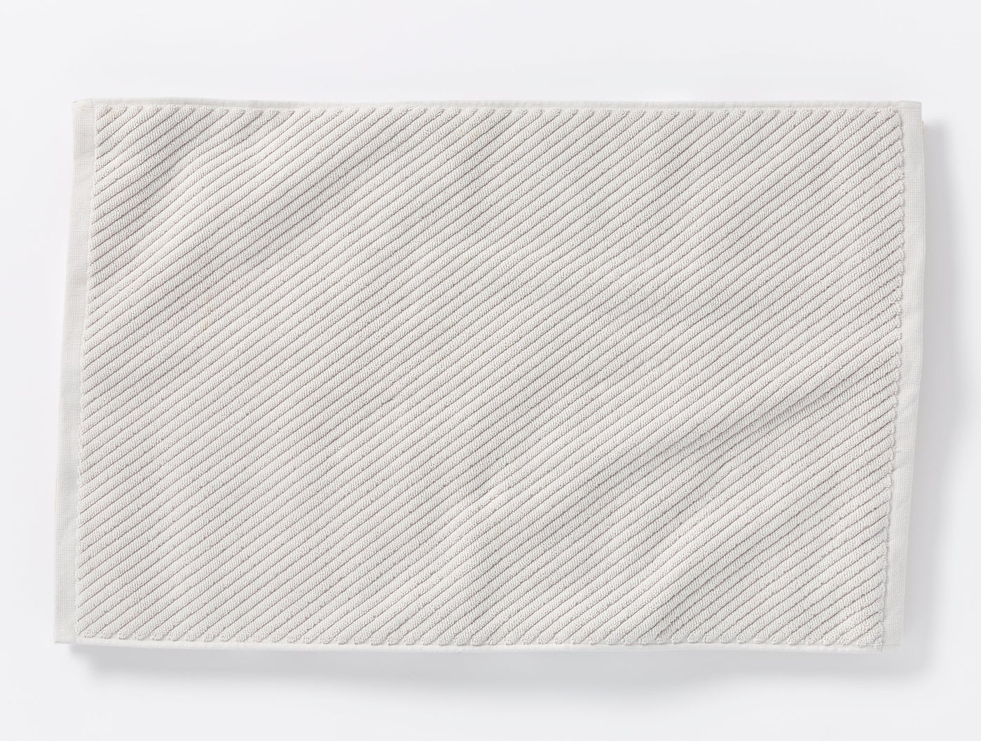 Coyuchi Air Weight bath rug laid flat, showing diagonal twill weave texture in white.