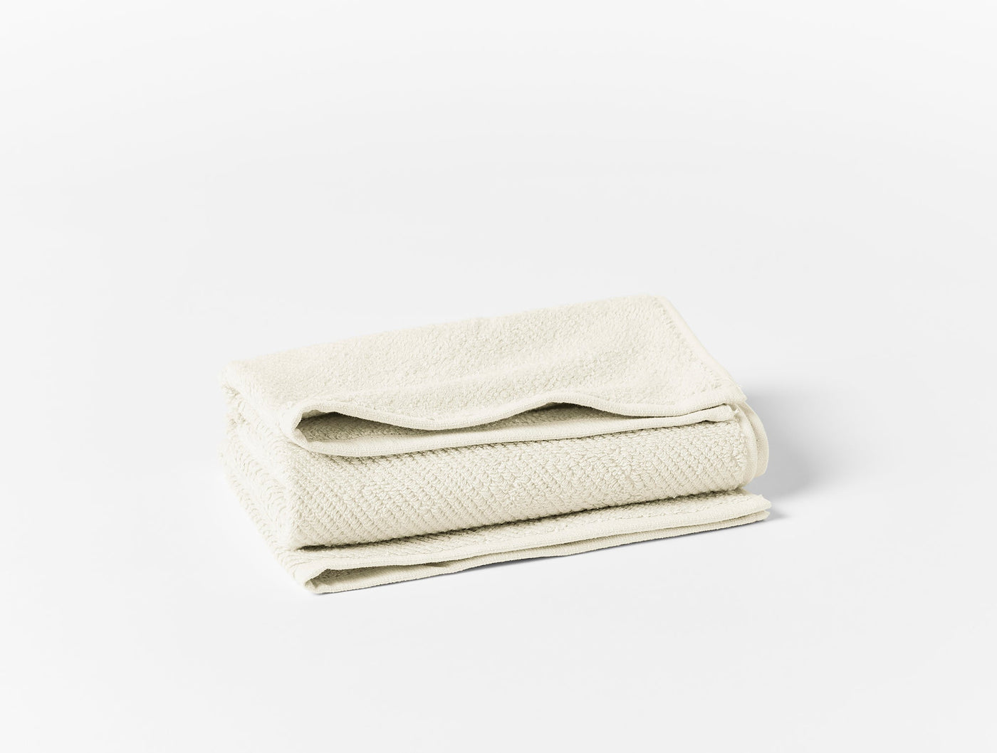 Folded ivory cotton towel set showing herringbone weave texture against white background.