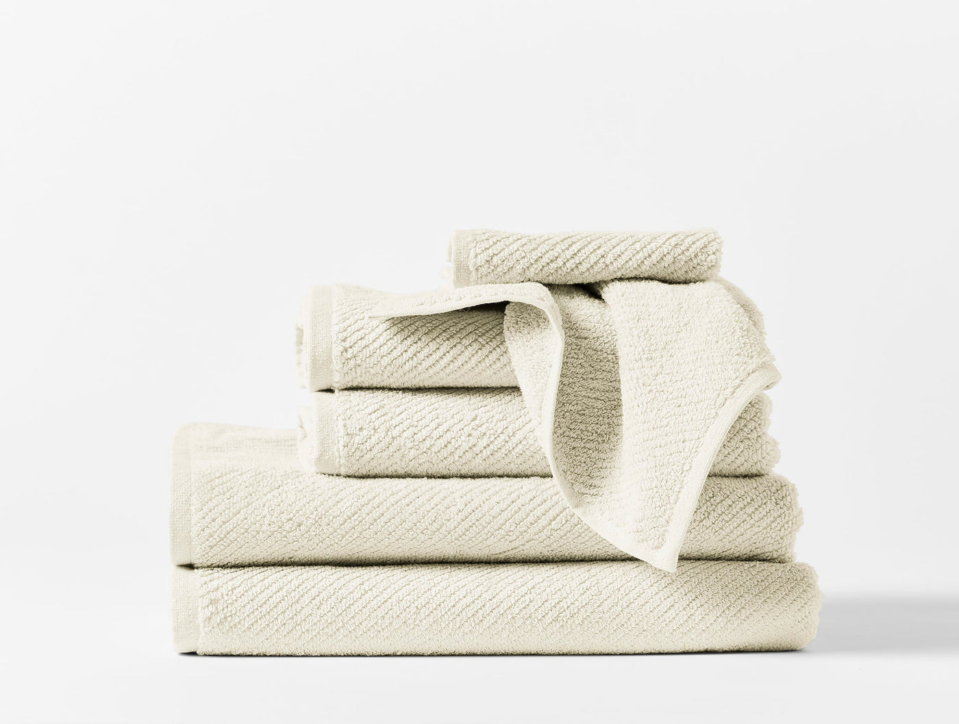 Stacked ivory Coyuchi Air Weight towel set showing varied sizes with ribbed texture detail.