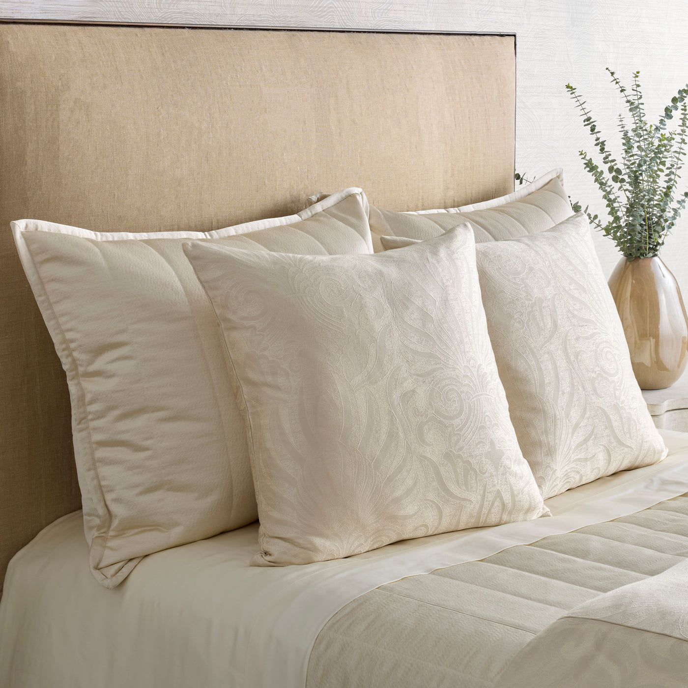 Ivory matelassé euro shams with floral quilting styled on a neutral bed.