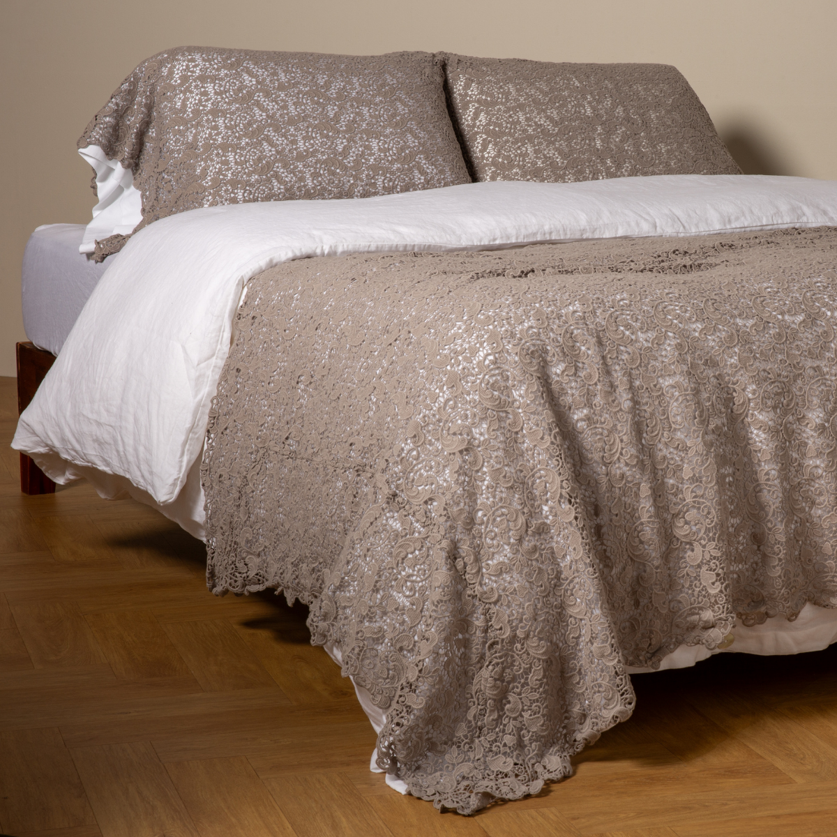 Fog Allora bed scarf draped over white duvet, lace-textured fabric on wood-framed bed.