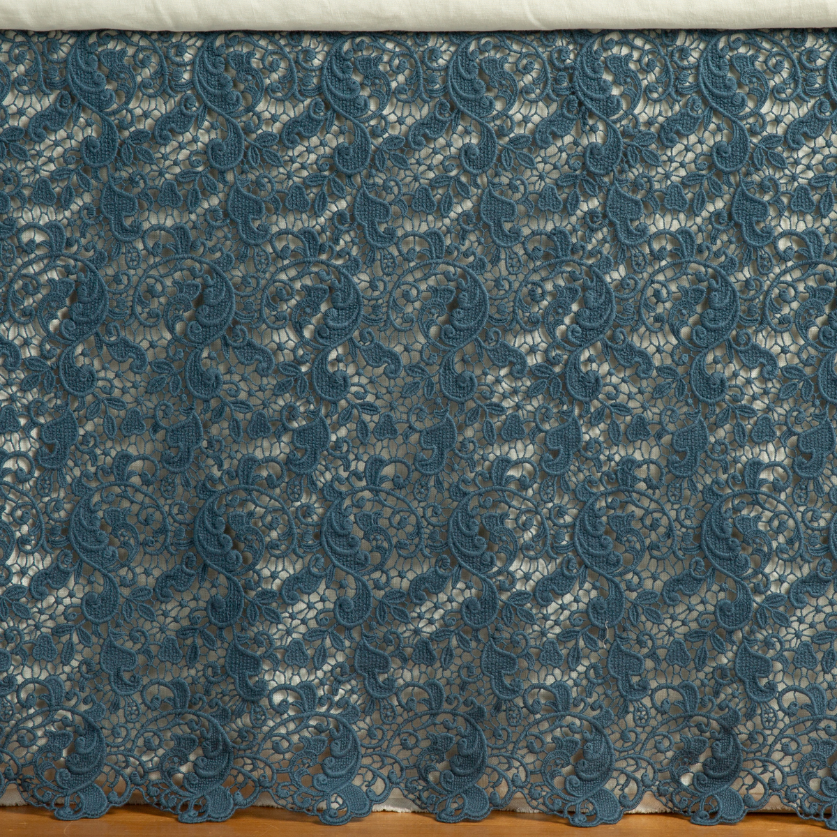 Midnight lace bed skirt with scalloped hem, floral scrollwork pattern draped against bed frame.