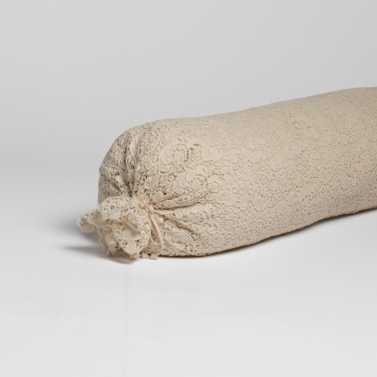 Natural lace bolster throw pillow with gathered end tie detail, angled side view.